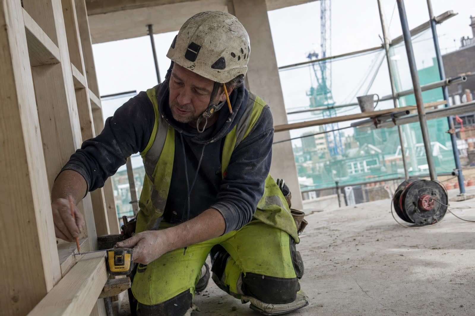 A carpenter marking out a timber stud partition on a London site